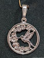 Front view of silver pendant showing hummingbird and floral wreath design inside circular frame