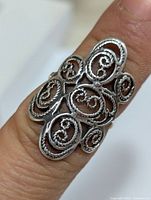Close-up of silver filigree ring on finger showing ornate swirl patterns and openwork design.