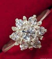 Close-up top view of silver ring showing central and surrounding clear gemstones in floral arrangement.