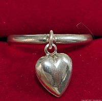 Close-up of the polished silver ring with a hanging heart-shaped charm on a red velvet background.