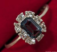 Close-up of the silver ring showing rectangular blue gemstone and clear surrounding stones on a silver band.