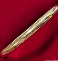 Close-up side view of slim silver ring on red background showing polished finish and smooth band surface.