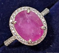 Close-up side-angle photo of the ring showing the oval ruby center set in four prongs and surrounding cubic zirconia halo.