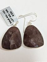 Pair of silver earrings with large teardrop-shaped dark purple faceted sapphires, showing front and side angles.
