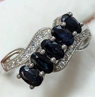 Close-up image of top of sterling silver ring showing five oval dark blue sapphires and small round cubic zirconia accents in the band.