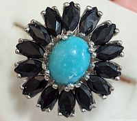 Close-up front view showing oval turquoise stone surrounded by marquise-shaped dark blue sapphires in silver setting.
