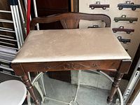 Full view of antique wooden seat with upholstered beige cushion and turned legs.