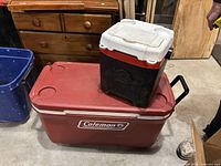 Large red Coleman cooler with smaller black and white cooler on top, showing size comparison and condition.
