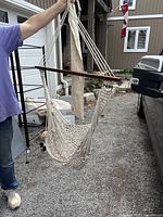 Hanging chair hammock made of woven cream-colored rope with wooden spreader bars, shown held up by a person outdoors.