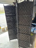 Three-panel dark brown wicker room divider standing upright, showing the woven pattern and hinged panels.