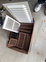 Box containing 10 brown heat vents, 1 white wall vent, and 1 white ceiling vent