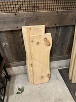 Two live edge wooden shelf boards leaning against a wooden wall, showing natural wood grain, knots and one live curved edge each.