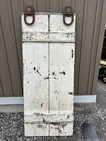 Front view of an old white wooden barn door with two large metal sliding hinges attached at the top. The door shows signs of use with paint chipping and scratches.