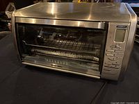 Closed toaster oven with visible front panel with buttons and digital display on right, stainless steel finish.