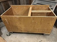 Photo of large utility storage box made from plywood on steel rollers in a garage or workshop setting.