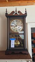 Front angled view of wooden mantle clock showing clock face and pendulum