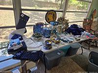 Wide shot of a table displaying assorted blue and white Christmas decorations with stockings, trays, pine cones, and ornaments arranged over a white cloth.