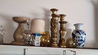 Photo of coordinated tabletop decor including candlesticks, amber glass small globes, glass bottle with stopper, large cream pillar candle, and a blue and white ceramic vase on a shelf