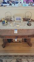 Wide view of wooden table with lace runner displaying multiple angel figurines, wire baskets, framed picture, and small container.