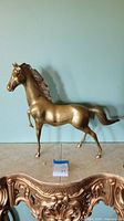 Front side view of the brass horse sculpture showing detailed mane and raised foreleg