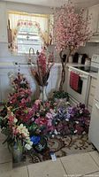 Full view of the assortment of artificial flowers, arrangements, and tall cherry blossom tree in decorative pots and vases in a kitchen corner