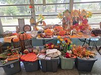 Full display of assorted fall themed decorations including scarecrows, pumpkins, floral wreaths, and various fall leaves and fabric pieces arranged on tables and storage bins.