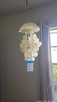 Full view of hanging white Capiz shell chime lit by natural light near window
