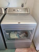 Full front view of silver dryer with clothes visible inside drum