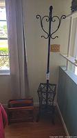 Full view of the metal coat rack with umbrella stand alongside wooden magazine rack by a window.