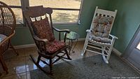 Two wooden rocking chairs placed near a window with a round glass top side table between them, showing the general lot contents.