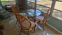 Rattan round table with clear glass top and four matching rattan chairs with lattice backs and beige seat cushions