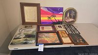 Full view of all assorted small wall decor items arranged on a table showing variety including framed plaques, tapestry, canvas painting, and metal sconce