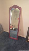 Full view of full length wooden framed mirror resting against wall on carpeted floor.