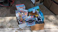 Box of assorted teaching materials including language books, flashcards, educational games, and teaching charts in an open cardboard box placed outdoors.