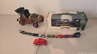 Photo showing a vintage brown toy car, a line of ten small assorted toy vehicles, and a boxed GM Motor Max 1950 Chevy Bel Air model car.