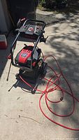 Full view of Troy-Bilt pressure washer unit with red hose coiled beside it showing overall condition