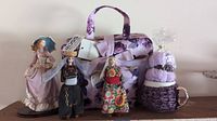 Photo showing Elizabeth Tracy travel set with purple floral case and three decorative dolls including porcelain and vintage cultural dolls, and purple crocheted mug cover with matching mug.
