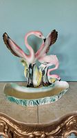 Front view of vintage ceramic flamingo figurine with two flamingos with outstretched wings and a smaller flamingo in a decorative base.