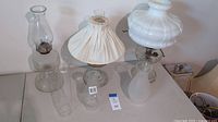 Overview of all three vintage oil lamps, showing glass bases, chimneys, and white glass shade with fabric cover on one lamp.