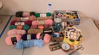 Photo showing assorted yarn skeins, sewing thread, buttons, tins, scissors and sewing supplies arranged on a table