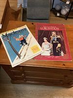 Both magazines displayed on wooden surface: Macleans magazine with skier cover illustration and Coronation souvenir guide with photo of King George VI and Queen Elizabeth
