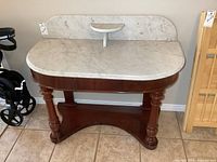 Front view of antique entrance table with white marble top, wooden base, turned legs, small drawer under marble surface, and raised marble backsplash with small shelf.