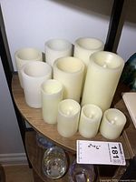 Photo showing ten cream/ivory colored battery powered candles of varying heights (2 to 6 inches) placed on a wooden surface in a group.