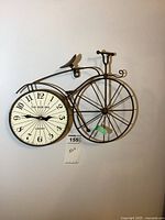 Metal bicycle wall clock with front wheel as clock face, bronze finish, cream background clock face with black numbers and hands.