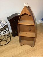 Front view of the wooden boat-shaped wall shelf showing three shelves and natural wood finish with reddish-brown trim.