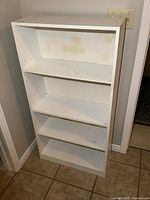 Front view of white melamine bookshelf showing four shelves and minor discoloration on back panel.