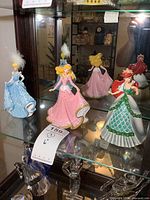 Wide shot of three Bradford Exchange Disney Princess figurines including Cinderella, Aurora, and Ariel displayed on a glass shelf.