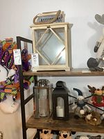 Set of three lantern candle holders on wooden shelf, surrounded by plush toys and Halloween decorations.