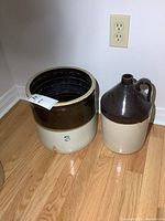 Photo of the 3 gallon crock and 1 gallon jug side by side on wood floor against white wall.