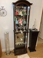 Front view of the curio cabinet with glass sides, mirrored back, and interior figurines for scale and display context.